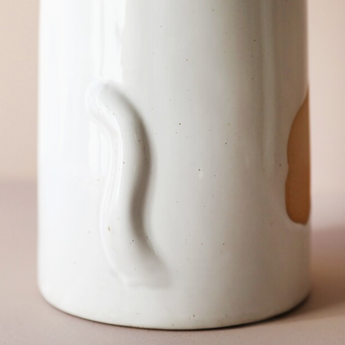 White ceramic cat vase with beige spots, pointy ears, and curly tail.