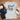 Gray t-shirt with 'one cat short of olazy' text, paired with jeans and a book on a white background