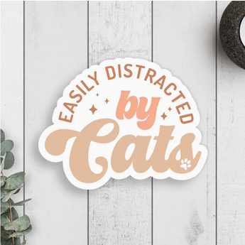 A sticker featuring the words "Easily Distracted By Cats" in playful orange print on a white background.