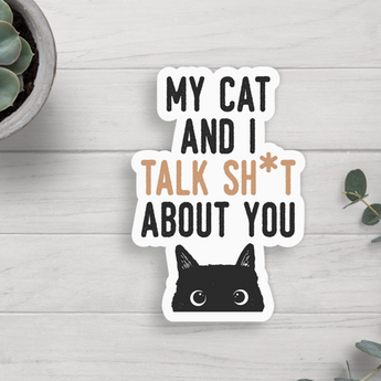 A sticker featuring the words "My Cat And I Talk Sh*T About You" in black print on a white background above a peeking black cat face looking at you.