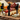 Three black cat-shaped cheese knives with silver blades are arranged on a wooden charcuterie board surrounded by crackers, grapes, cheese, and cured meats.