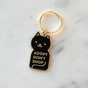 Adopt Don't Shop Keychain featuring a black cat with "Adopt Don't Shop" stamped in gold.