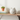 A round, cat-shaped ceramic container or decor piece with a distressed off-white finish and small black facial details, displayed on a wooden shelf next to stacked books and a small potted succulent.