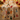 A festive Christmas table runner or tea towel with a cream background and a colorful print of holiday ornaments, gingerbread men, snowman, cats, candy canes, and Christmas trees, draped over a wooden surface with warm bokeh holiday lights in the background.