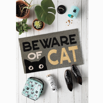 A humorous doormat with a black cat's face peeking out from behind the phrase "Beware Of Cat," set against a grey background.