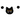 A black felt cat head garland with yellow eyes, a pink nose, and white whiskers, hanging on a string with two black felt balls on each side against a white background.