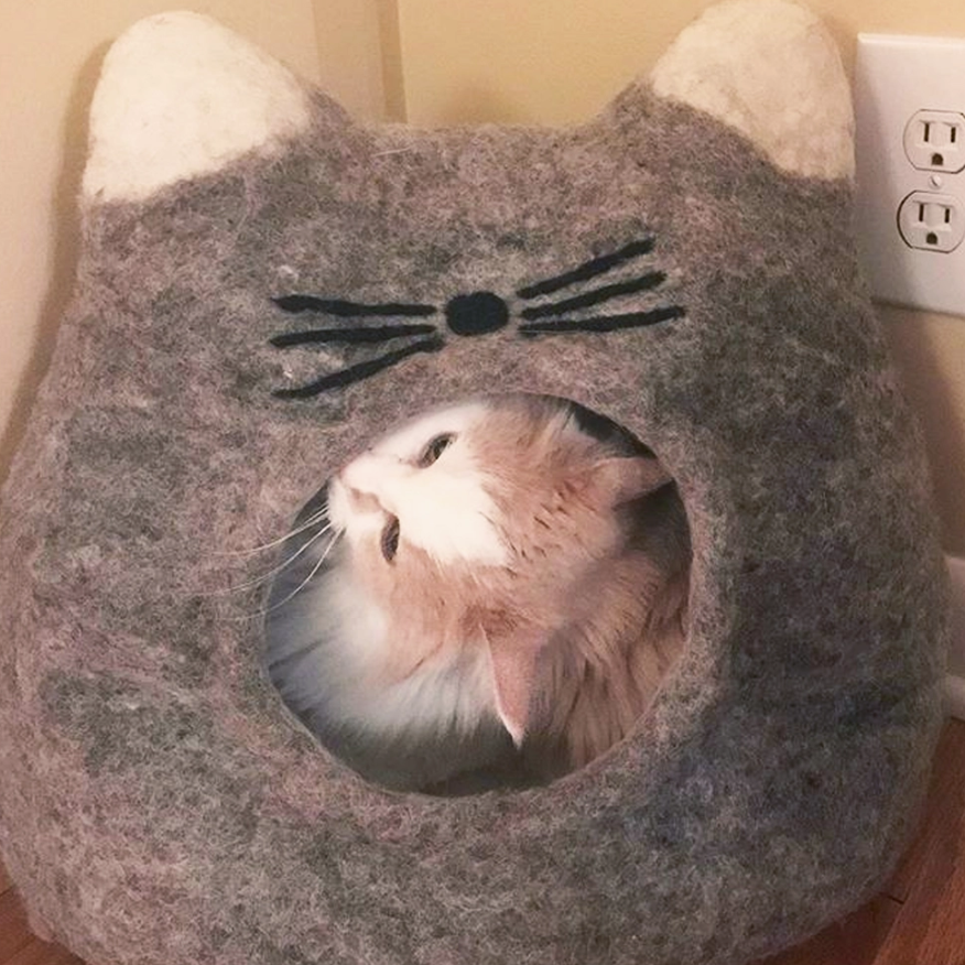 Happy cat relaxing inside cozy grey pet cave, surrounded by comfort and safety.