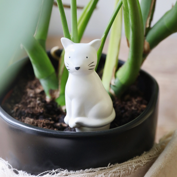 White ceramic cat-shaped plant watering spike inserted in a plant pot.