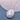 An oval silver locket necklace featuring a light blue and white cameo-style cat pendant, displayed on a textured blue fabric with a pale stone prop in the background.