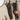 Two long black cat-face cleaning gloves hanging on a bathroom towel rack, with a hand stretching one glove to show its flexibility. A beige tiled wall, a round mirror edge, and a white pump bottle are visible in the background.