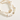 Two beaded stretch bracelets on a warm cream background. One bracelet features white and cream striped shell-like beads with small gold spacer beads, and the other features round white beads spelling 'CAT MOM' with gold lettering, alongside a gold cat-shaped charm and a small gold heart.