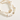Two beaded stretch bracelets on a warm cream background. One bracelet features white and cream striped shell-like beads with small gold spacer beads, and the other features round white beads spelling 'CAT MOM' with gold lettering, alongside a gold cat-shaped charm and a small gold heart.