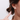 A close-up of a woman's ear wearing a small silver stud earring shaped like a cat's head with a white pearl center, against a light gray background.