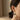 A close-up side profile of a woman wearing a dangling earring shaped like a black-and-white cat under a small umbrella, with gold-tone hooks and hooks.