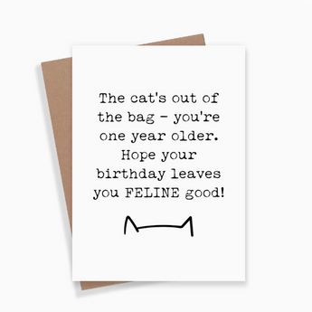A playful Cat's Out Of The Bag Birthday Card featuring a black cat head silhouette and the humorous message "The cat's out of the bag - you're one year older. Hope your birthday leaves you FELINE good." The card is printed on white cardstock with bold black print, measuring 5.5" by 4.25".
