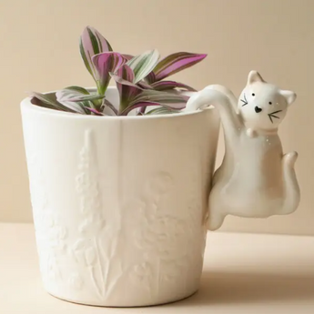 White ceramic cat-shaped planter hanger hanging off the edge of a flower pot.