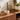 A white ceramic cat-shaped jewelry box with gold-rimmed glasses sits on a wooden console table, styled with gold jewelry, a gold-framed print, and a potted succulent in a warm, modern interior.