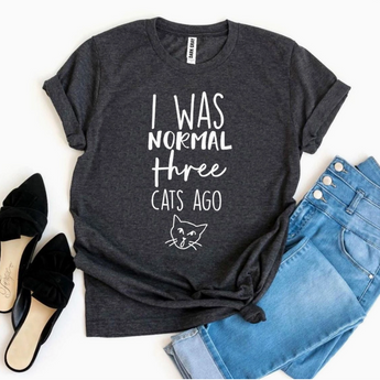 I Was Normal Three Cats Ago T-Shirt in dark heather grey with playful white font print and cat face graphic.