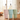 Three pastel-colored insulated tumblers with matching lids are lined up on a wooden table in a bright, softly blurred living room setting. Each tumbler has a straw with a small cat character on top.