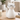 A white ceramic cat-shaped object with black wire eyeglasses, sitting on a light wood table in a softly blurred indoor setting.