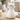 A white ceramic cat-shaped object with black wire eyeglasses, sitting on a light wood table in a softly blurred indoor setting.