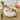 Cat lying on a round beige pet bed with flowers and a picture frame in the background.