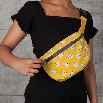 Mustard yellow hip bag with smiling white cat faces, front view.
