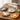 Four cat-shaped felt coasters in gray, white, orange, and yellow-orange are arranged on a wooden table beside a mug of tea, a green coffee mug, an open book, and glasses in a cozy indoor setting.