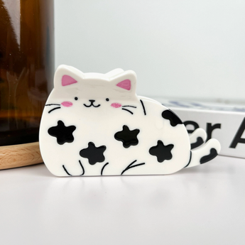 Happy cat-shaped hair claw with black spots, white plastic design, and a smiling face, 3.7 inches.